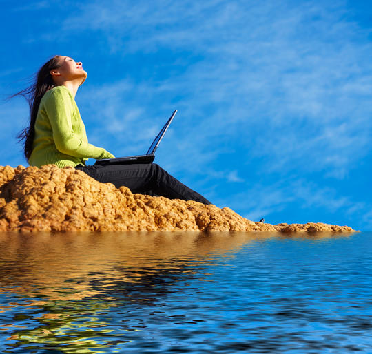Kvinne sitter ved vannkanten med en laptop i fanget.