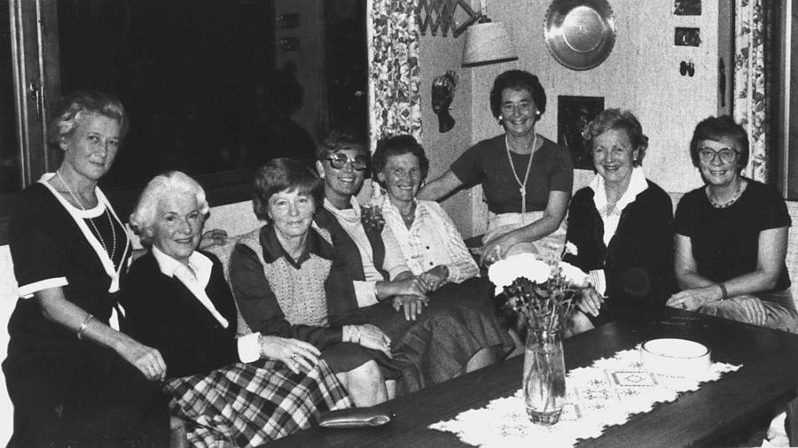 8 kvinner sitter sammen i en sofa og smiler til fotografen.